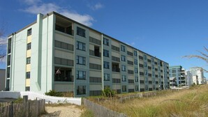 A multi-story building with balconies, a sandy path, and a wooden fence. - Cozy, yet spacious 2 bedroom oceanfront condo with free WiFi and a stunning view of the ocean located midtown just a few steps to the beach! (Ocean City)