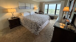 A bedroom with a large bed, two bedside tables with lamps, a dresser, and a window with a view. - Cozy, yet spacious 2 bedroom oceanfront condo with free WiFi and a stunning view of the ocean located midtown just a few steps to the beach! (Ocean City)