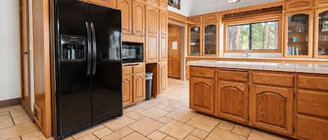 A kitchen with wooden cabinetry, a black refrigerator, a microwave, and a ceiling fan.