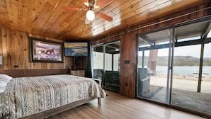Un dormitorio con cama, techo de madera y un amplio ventanal con vistas a un lago.