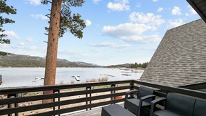 Una terraza con mobiliario de mimbre que da a un lago con barcos, rodeada de árboles y colinas.