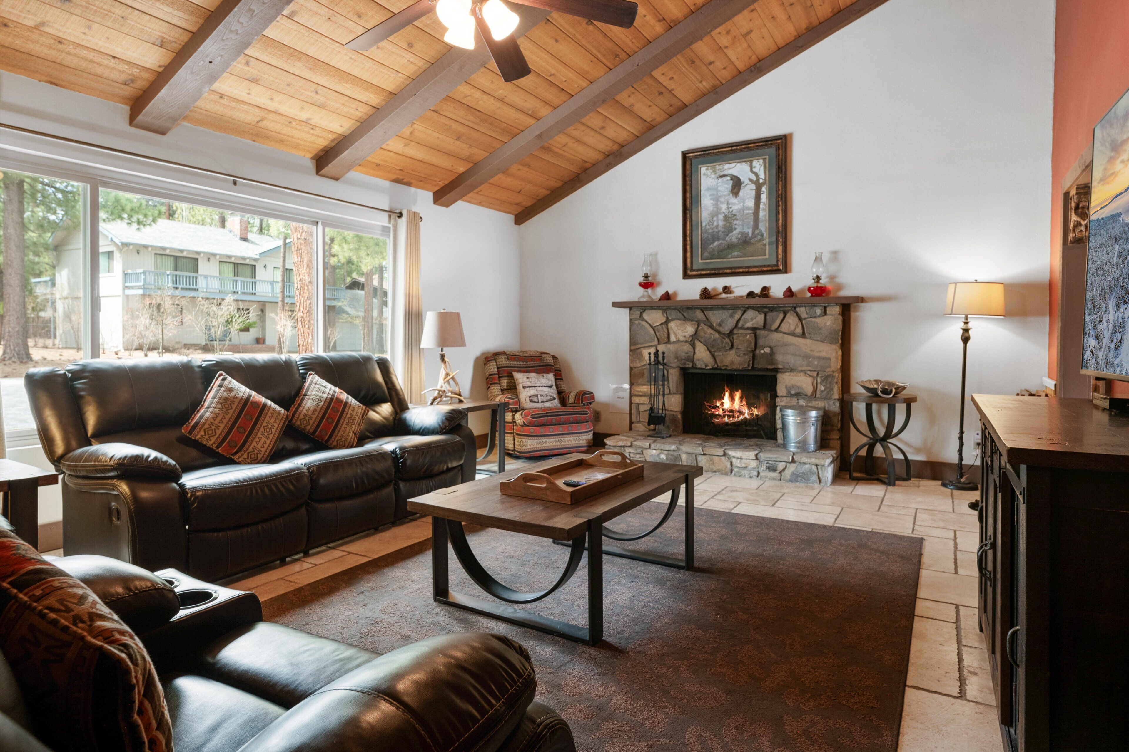 A cozy living room with a stone fireplace, leather sofas, and a wooden ceiling.