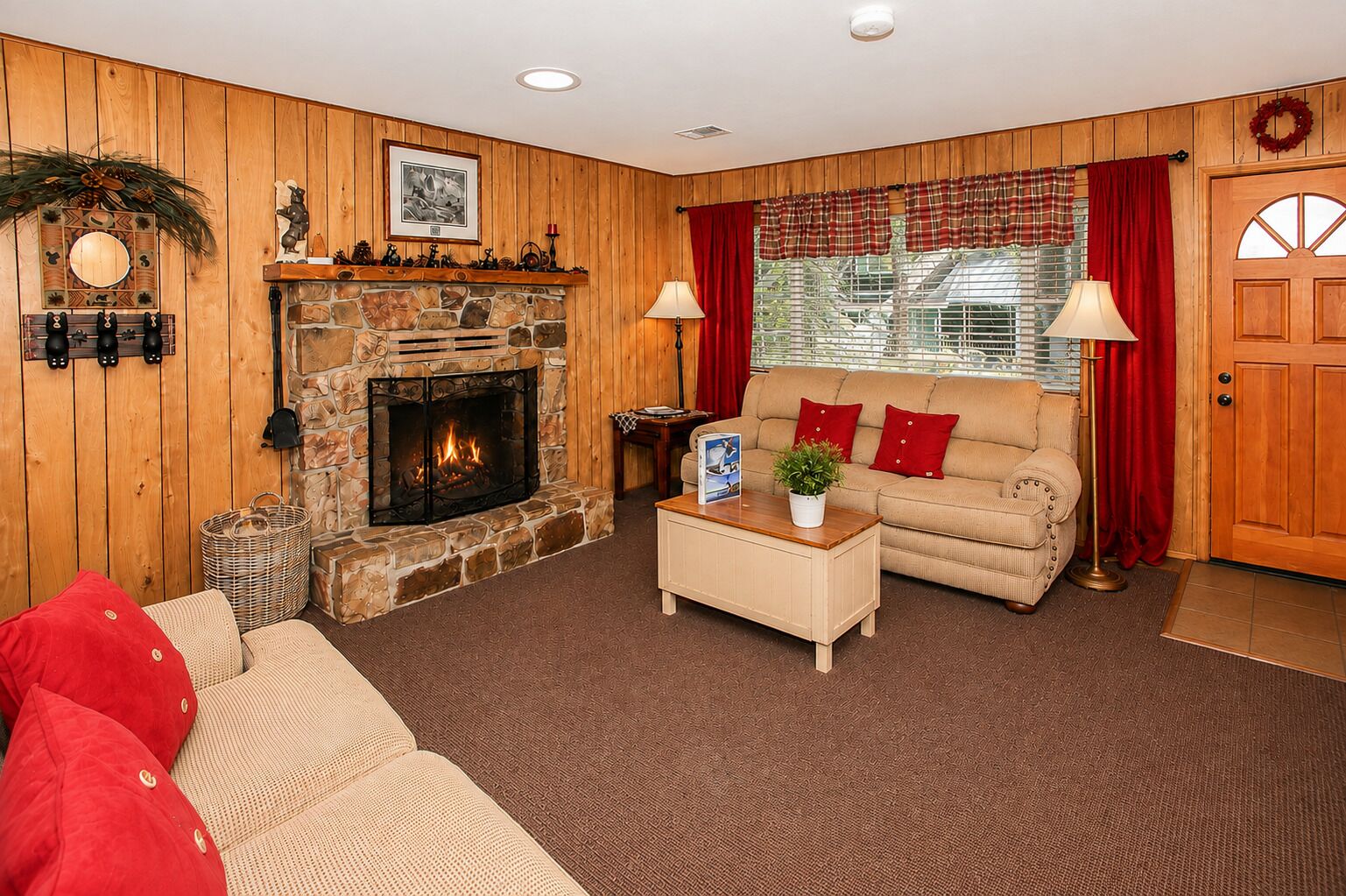 A cozy living room with a stone fireplace, a sofa, a coffee table, and a window with curtains.