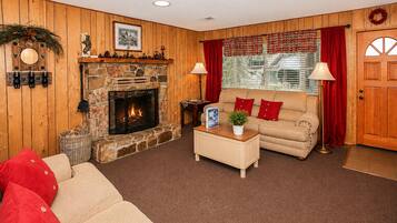 A cozy living room with a stone fireplace, a sofa, a coffee table, and a window with curtains.