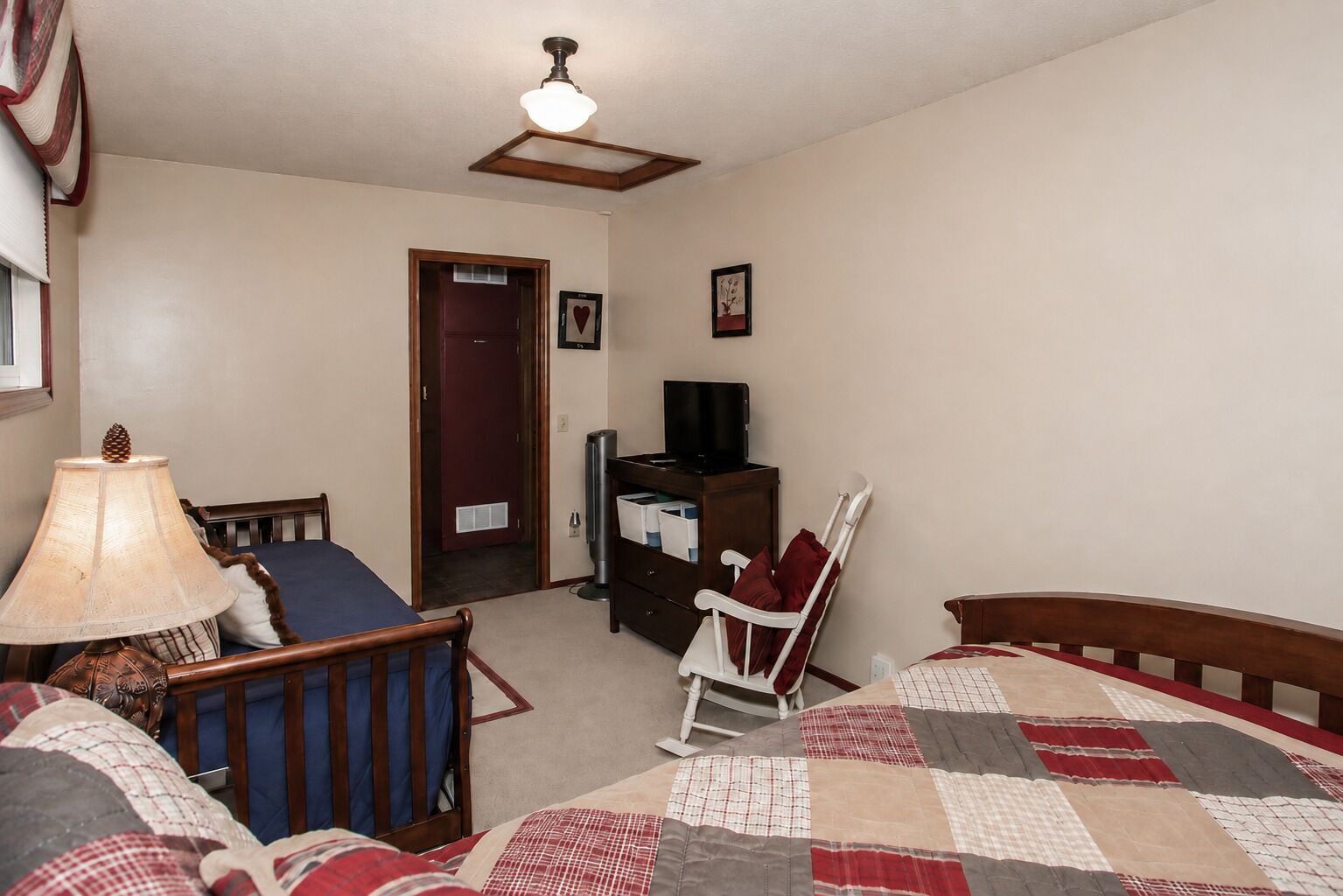 Un dormitorio con cama, una silla, un escritorio, un televisor y una puerta.