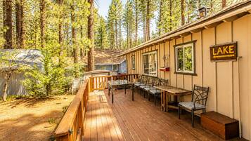 A deck with outdoor seating, surrounded by tall trees, and a sign indicating 'LAKE' to the right.