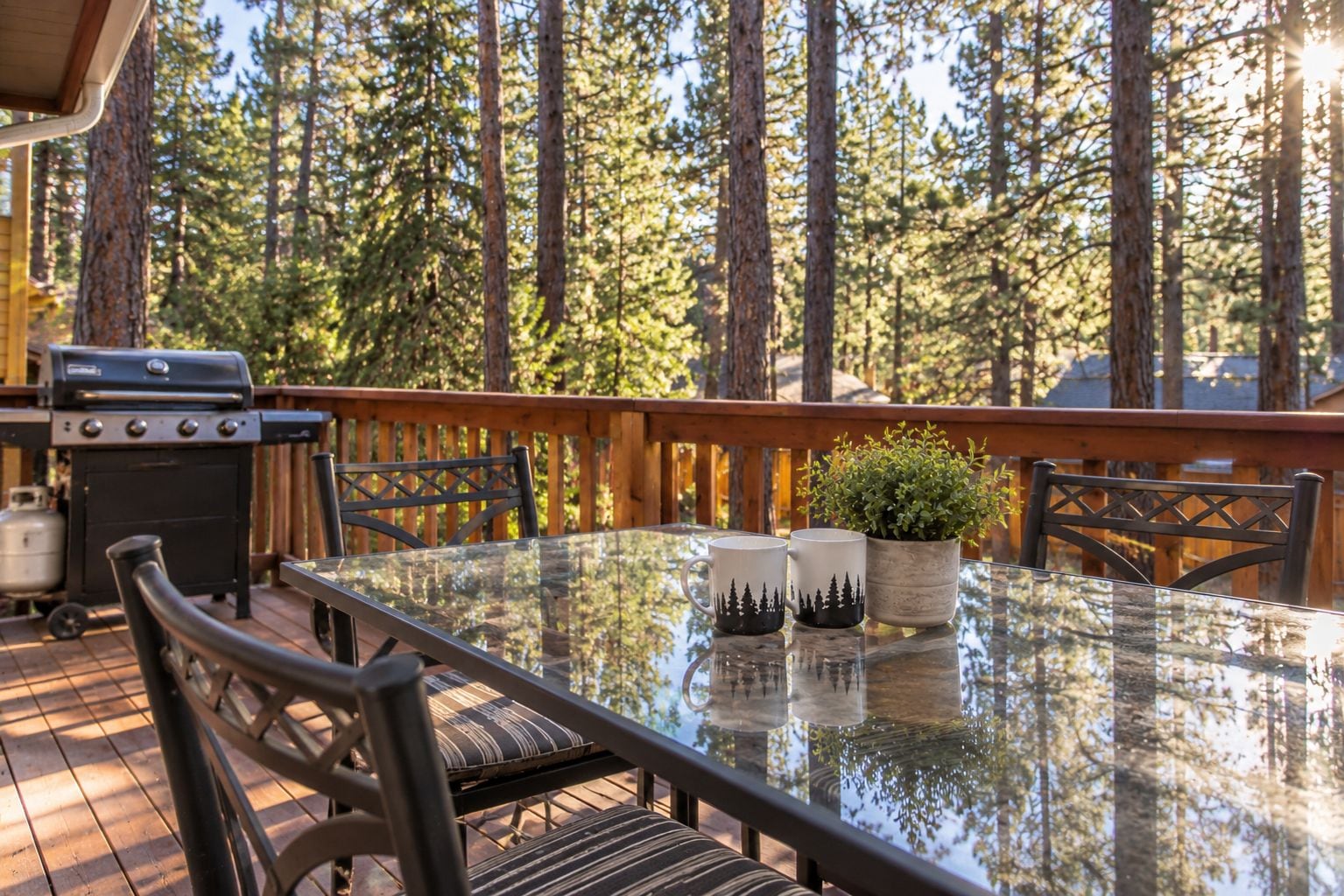 An outdoor deck with a glass table, chairs, a grill, and a potted plant.