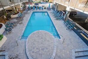 Una piscina rectangular con una solana azulejada, rodeada de sillones de descanso y una pequeña mesa con sombrilla.