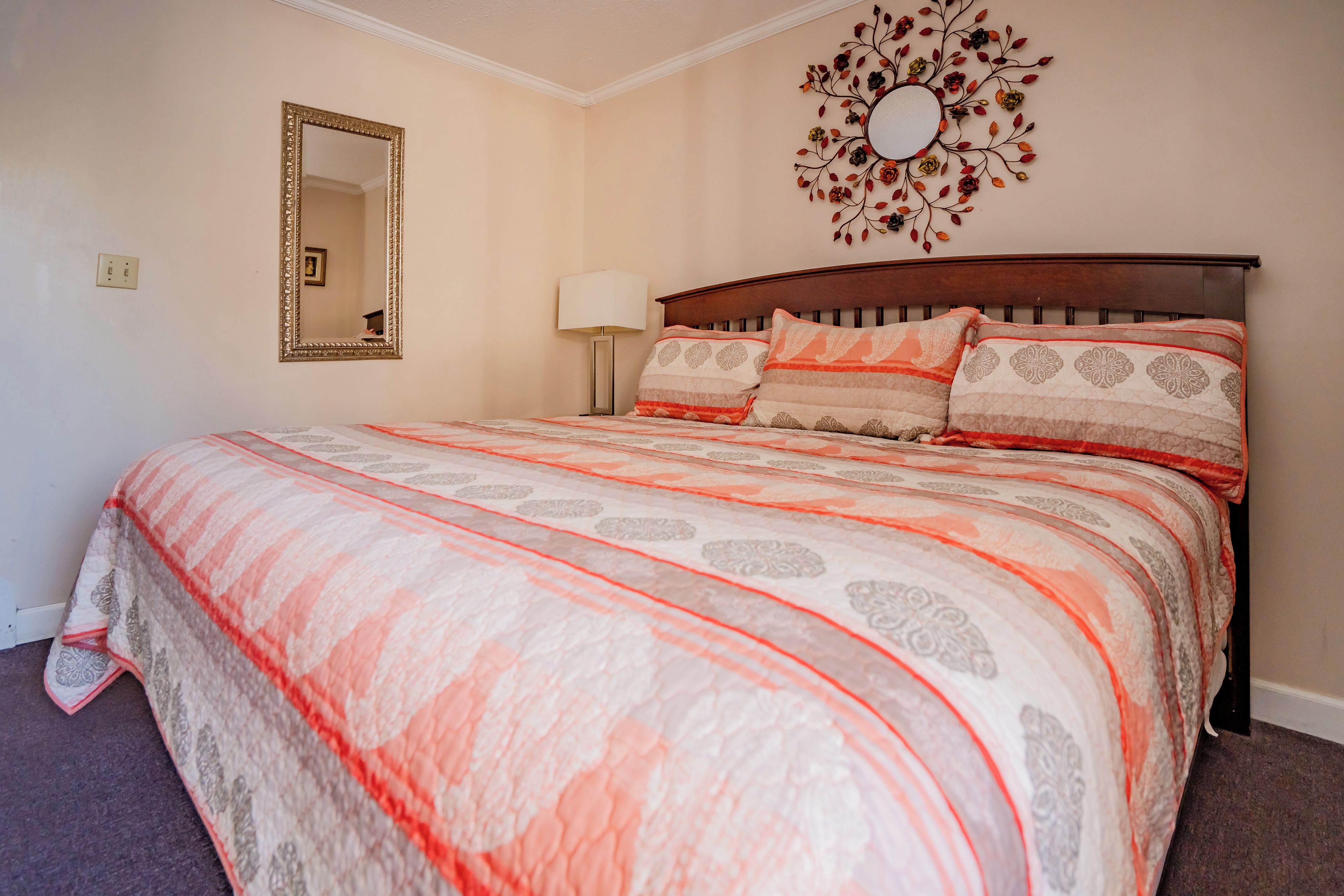 A bedroom with a bed, a mirror, a wall-mounted decorative piece, and a lamp.