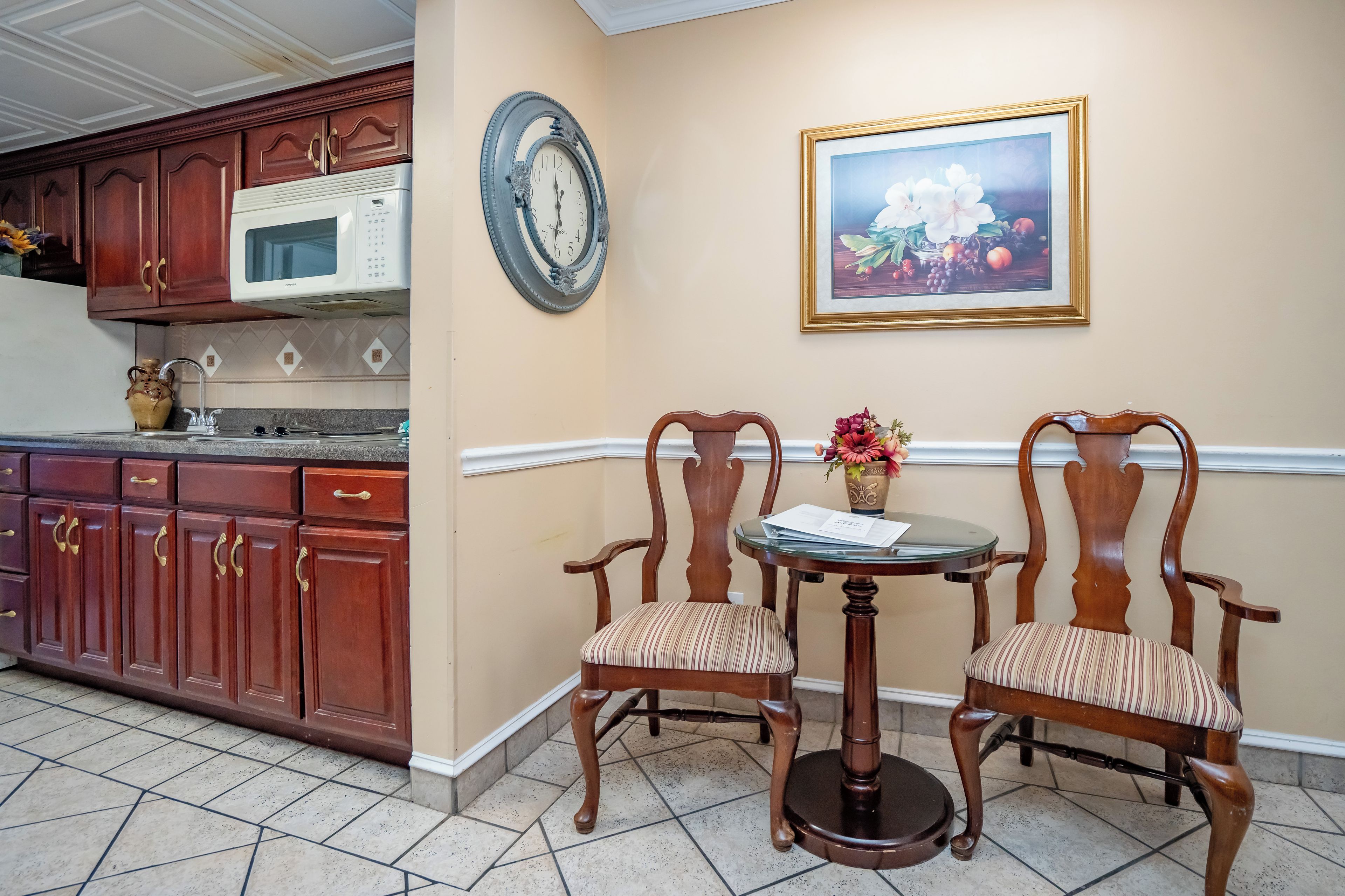 A kitchen with wooden cabinets, a microwave, a wall clock, and a framed painting.