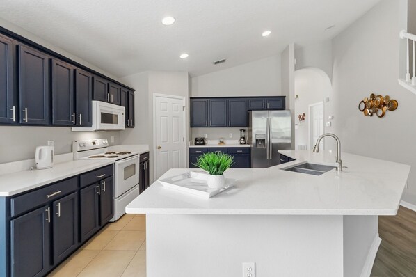 A modern kitchen with dark cabinets, white countertops, a central island, and a stainless steel refrigerator.