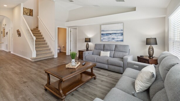 Un salon spacieux avec un canapé gris, une table basse en bois et un escalier menant à un autre niveau.