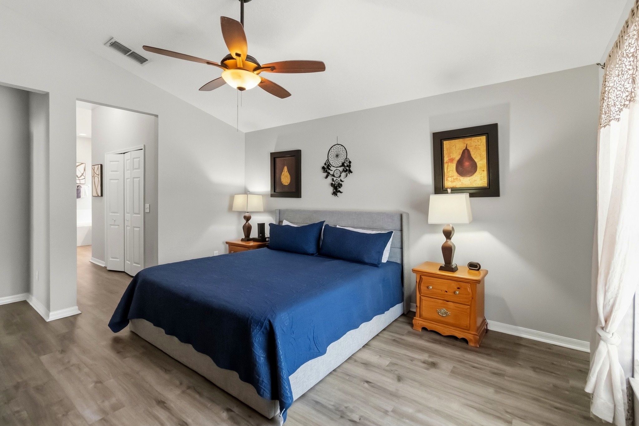 A bedroom with a bed, two bedside tables, a ceiling fan, and artwork on the walls.