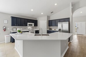 Una cocina moderna con armarios oscuros, una isla central, electrodomésticos de acero inoxidable y encimera blanca.