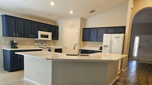Une cuisine moderne avec des meubles de couleur sombre, un îlot central blanc et un réfrigérateur en acier inoxydable.