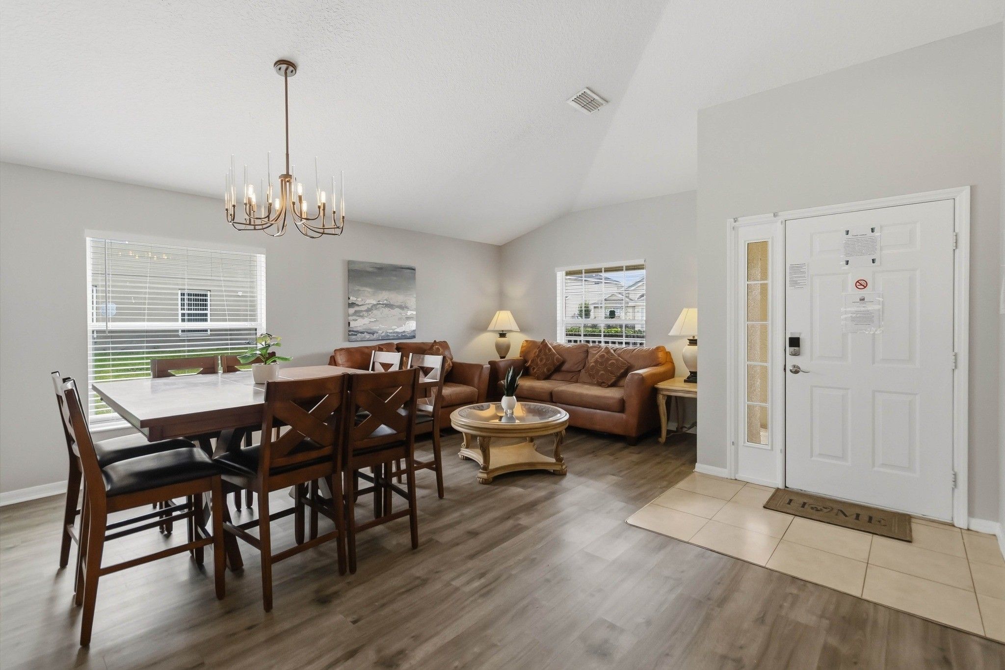 A spacious living area with a dining table, chairs, a sofa, and a coffee table. There is a door with a doormat on the floor.