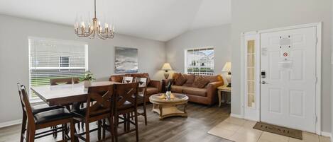 A spacious living area with a dining table, chairs, a sofa, and a coffee table. There is a door with a doormat on the floor.