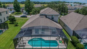 Un quartier résidentiel doté d’une grande piscine couverte par une structure en verre, entourée de maisons et de verdure.