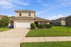 A two-story residential house with a garage, a well-maintained lawn, and a clear sky.