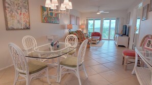 A spacious living room with a glass dining table surrounded by white wicker chairs, a red sofa, and a television. - Top Floor View With Bottom Floor Pricing...... (Sanibel)