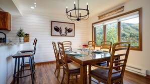 A dining area with a wooden table, chairs, and a chandelier. There is a window with a view of a landscape. - RA517 | Nice Furnishings | Pool and Hot Tub Access | Winter Shuttle (Steamboat Springs)