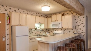 Eine Küche mit Holzausstattung, einem weißen Kühlschrank, einer Mikrowelle, einem Spülbecken und einer Theke mit Hockern.