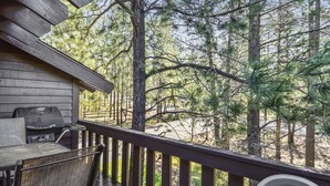 Une terrasse en bois avec un barbecue et des sièges d’extérieur, entourée de grands pins.