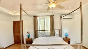 Een hemelbed met plafondventilator, een houten garderobe en een nachtkastje met lamp.