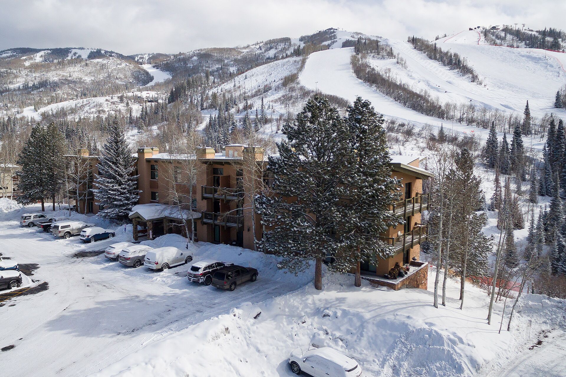 A snow-covered building with multiple floors, surrounded by snow-covered trees and a ski slope in the background.