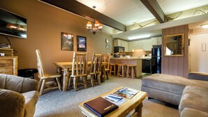 Un salon chaleureux avec une cheminée, des meubles en bois et un coin repas donnant sur une cuisine en arrière-plan.