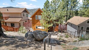 A two-story wooden cabin with a balcony, surrounded by trees and a rocky landscape.