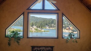 A room with a sloped ceiling, a ceiling fan, and three large windows offering views of a lake and surrounding landscape.