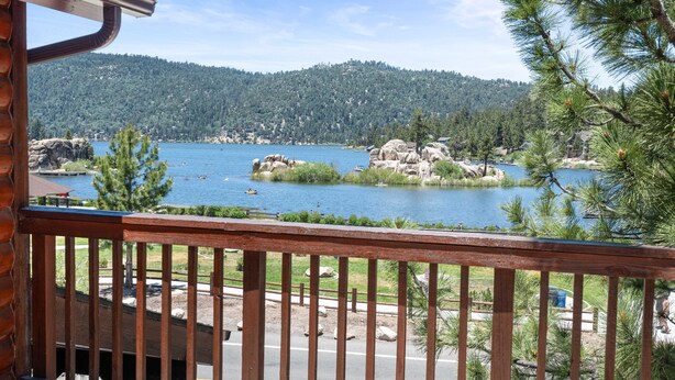 A view from a wooden balcony overlooking a lake with rocky islands, surrounded by dense forest and a clear sky.