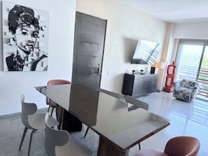 A modern dining area with a glass-top table, grey chairs, a grey cabinet, and a large abstract painting.