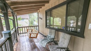 Une terrasse en bois avec deux chaises et une table, une grande fenêtre et une porte portant un numéro.