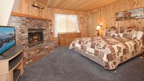 Une pièce chaleureuse avec une cheminée en briques, un lit recouvert d’une couverture à carreaux et un téléviseur posé sur un meuble en bois.