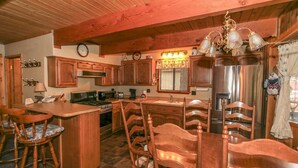 Une cuisine avec des meubles en bois, un îlot central doté de tabourets de bar, un lustre et des appareils électroménagers en acier inoxydable.