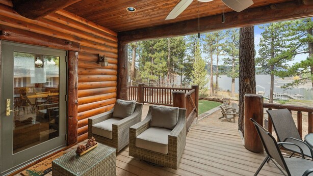 A log cabin with a wooden deck, wicker furniture, and a view of trees and water.
