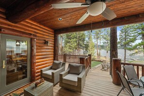 A log cabin with a wooden deck, wicker furniture, and a view of trees and water.
