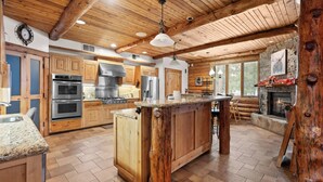 A spacious kitchen with wooden cabinets, a large island, and a stone fireplace.