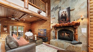 A log cabin interior with a fireplace, leather furniture, and a stone wall.