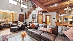 A spacious living area with a leather sofa, wooden staircase, and a kitchen in the background.