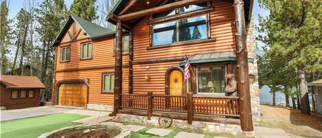 A log cabin with a stone foundation, a wooden porch, and a flag.