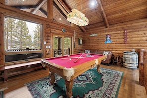 L’intérieur d’un chalet en bois, avec une table de billard, un banc, un tabouret de bar et une grande fenêtre.