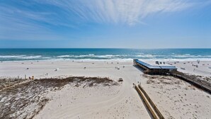 Ein Strand mit einem Holzsteg, einem Gebäude mit blauem Dach und dem Ozean im Hintergrund.