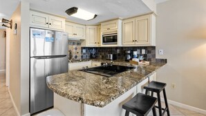 A kitchen with a stainless steel refrigerator, a microwave, a stove, and a granite countertop.