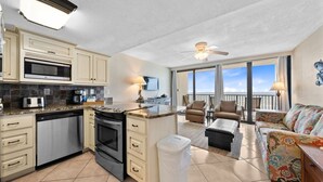 A spacious kitchen with a microwave, oven, and dishwasher, a balcony with a view, and a living area with a sofa and chairs.