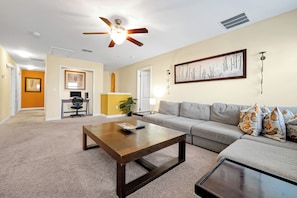 A living room with a ceiling fan, a sofa, a coffee table, and a television. - Champions Gate Pool Home | 3 King Suites | Game Room | Dog Friendly (Champions Gate)