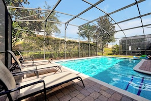 An indoor swimming pool with clear blue water, surrounded by a glass enclosure, and equipped with lounge chairs and a small play area. - Champions Gate Pool Home | 3 King Suites | Game Room | Dog Friendly (Davenport)
