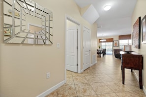 A hallway with a tiled floor, a wall-mounted mirror, and a door leading to another room. - Champions Gate Pool Home | 3 King Suites | Game Room | Dog Friendly (Davenport)